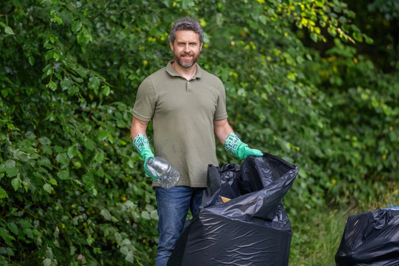 Eco volunteer. Garbage collecting in forest. Eco-friendly waste solutions. Volunteer collecting garbage, ecology. Man in rubber gloves with trash bag clean up garbage. Man collecting plastic trash.