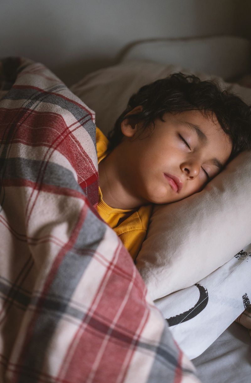 A young child sleeping peacefully in bed at home, covered with a blanket and resting on a pillow