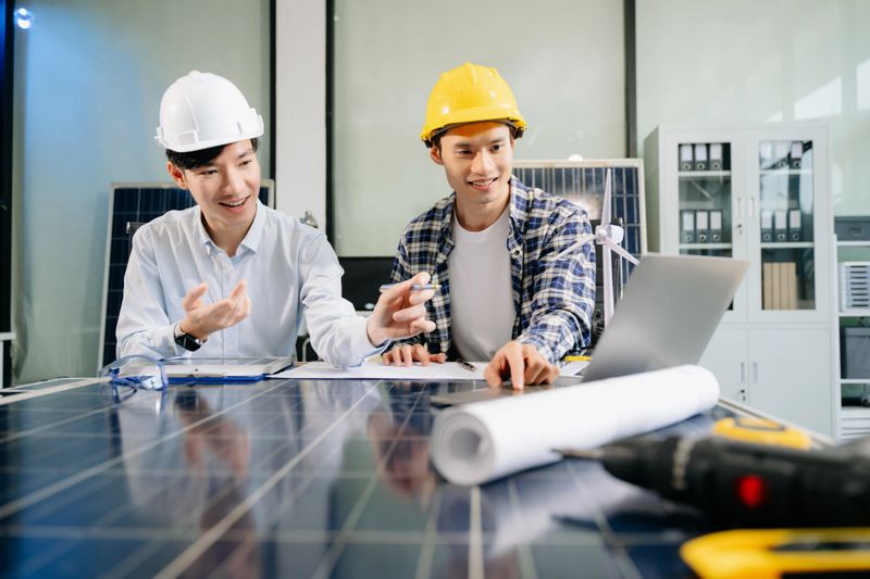 Two Asian engineers collaborate on solar and wind energy, driving clean innovation and sustainability. A vision of teamwork