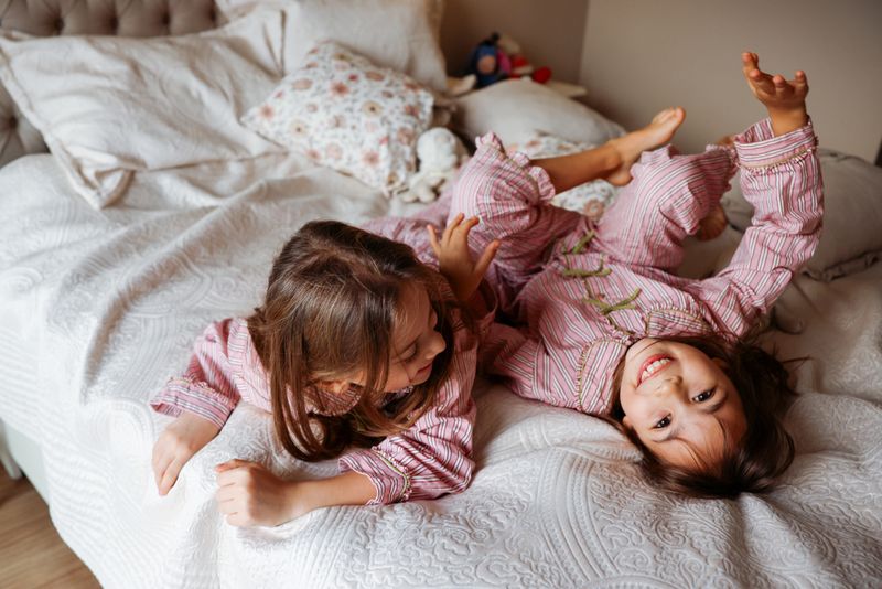 Sisters laugh and play together on mother's bed at home. Two girls lying on the bed and smiling at camera
