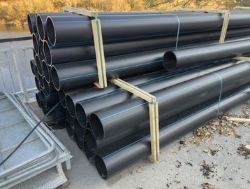 Stacked black plastic pipes with blue lines, secured with wooden frames.