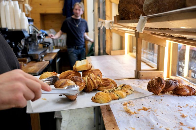 A worker tidying up a window display of pastries in an outlet shop for a small bakery selling artisanal bread, pastries and coffee in North London.