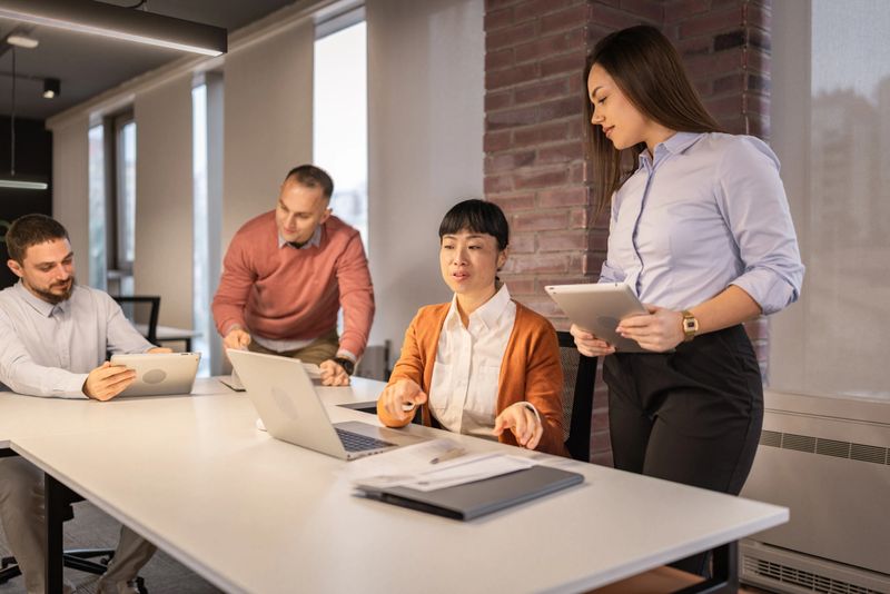 A group of multicultural  coworkers engage in a productive  business meeting  inside a bright, contemporary office with natural light, focusing on a documents and technology.