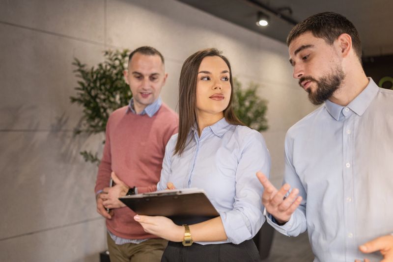 A team of young diverse professionals engage in a productive discussion while walking trough a bright, minimalist office hallway natural and soft artificial lighting