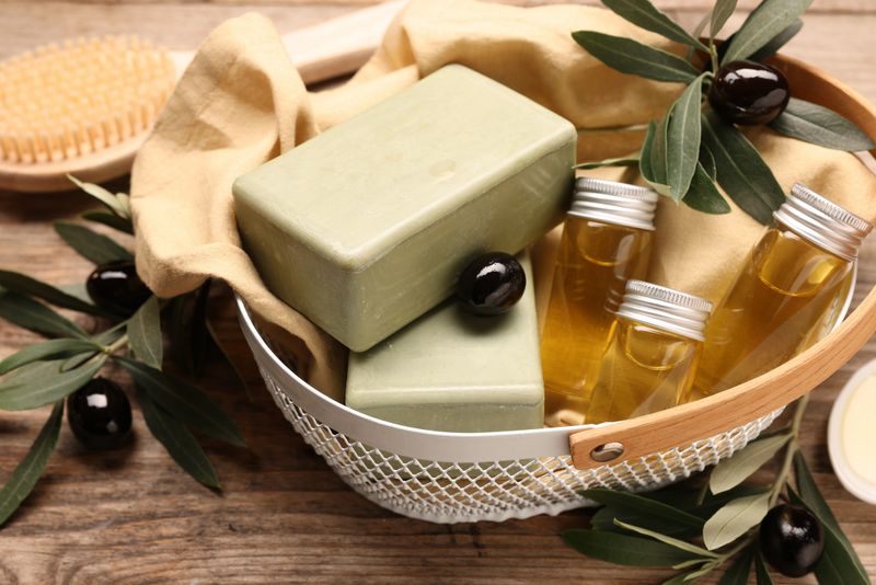 Natural soap bars, olives, oil and brush on wooden table, closeup