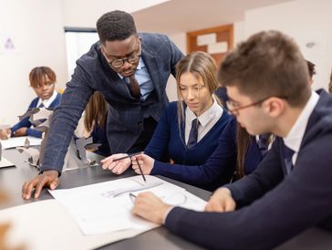Teacher helping students with sketches in a classroom setting.