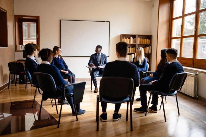 A group of individuals sitting in a circle in a well-lit room, participating in a therapy session led by a therapist. The atmosphere is professional and supportive.