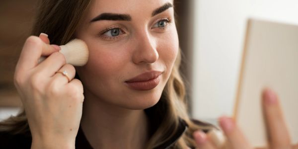 Woman applying makeup using a brush and mirror.