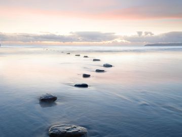 Stepping stones in calm water under a pastel sky.