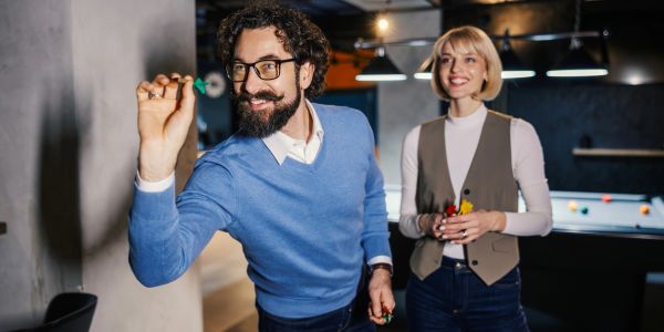 Man aiming to throw a dart while a woman watches and smiles.