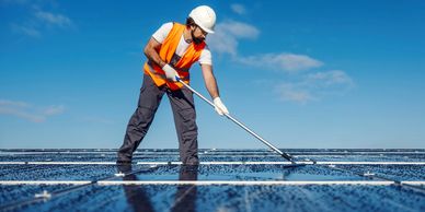 Worker cleaning solar panels under blue sky.