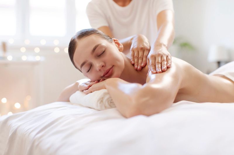 Smiling relaxed lady lying on massage table and receiving back massage in calm setting, free space