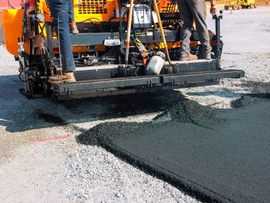 Machine paving fresh asphalt on a road under construction.