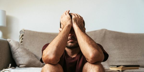 Man sitting on couch with hands covering his face, looking stressed.
