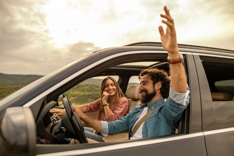 Happy couple driving car on scenic road, singing to music, feeling joy and freedom during golden hour