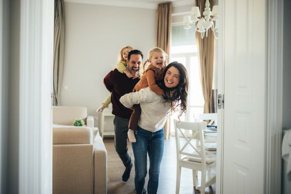 A joyful family playing indoors with parents giving piggyback rides to their children.