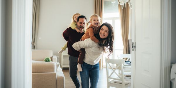 Happy family playing indoors with children on parents' backs.