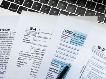 Tax forms W-4, 1040, and W-9 on a keyboard with a pen.
