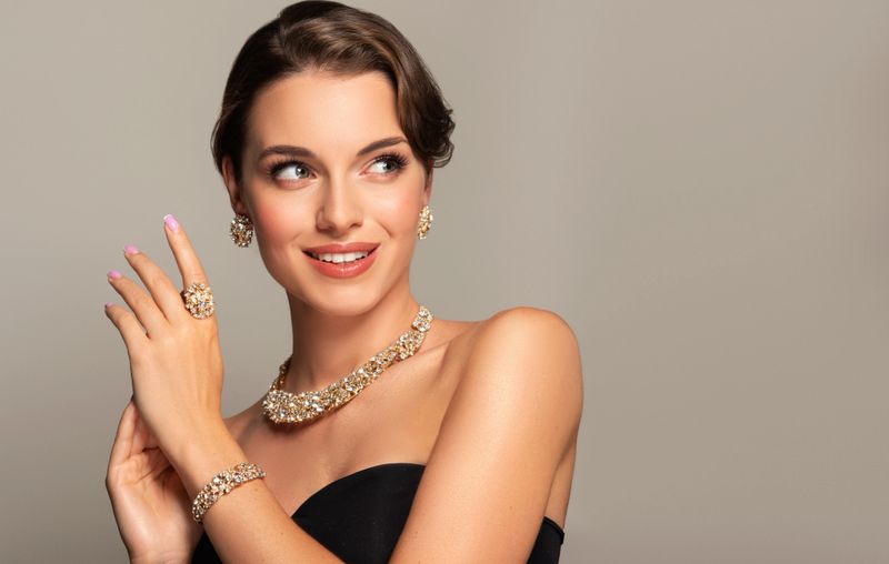Gorgeous young woman wiht misty look of green eyes dressed in elegant gilded with bright stones jewelry set. Makeup with rose lipstick, black eyelids and black eyeleshes on the face. Jewelry, makeup and woman beauty.