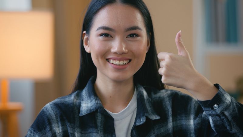Cheerful Asian Korean woman showing thumbs up smiling toothy dental clinic happy female girl patient indoors positive feedback approval gesture service dentistry advertisement health care satisfaction. High quality 4k footage