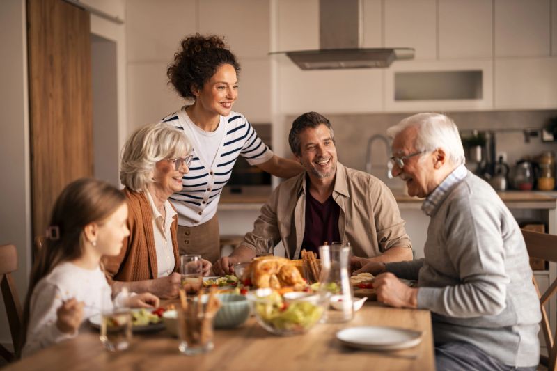 Multi-generational family happily celebrating a special occasion, sitting around a dining table, eating a delicious roasted turkey and sharing joyful moments and conversations at home