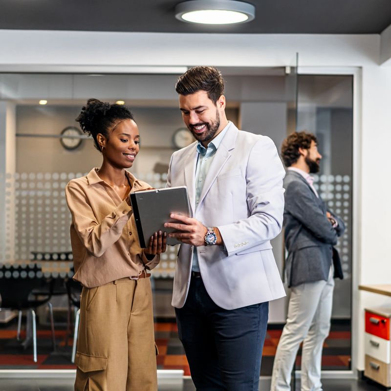 Diverse business professionals smiling, collaborating, and discussing work using a digital tablet in a modern office environment