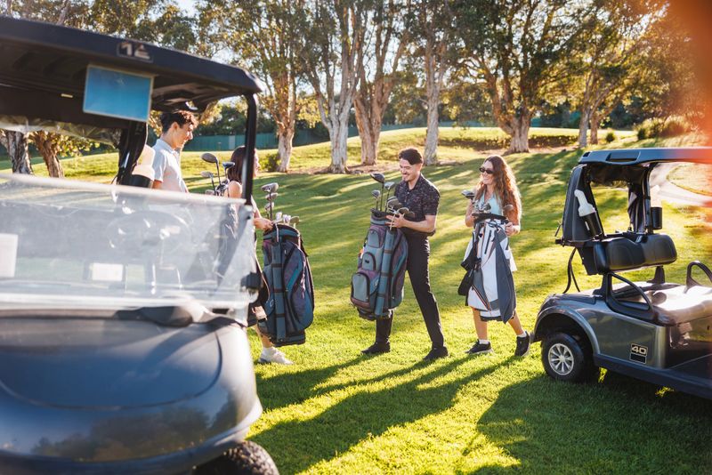 Caucasian young adults gathering and organizing golf gear on a sunny course, engaging in preparation for their game with visible enthusiasm and camaraderie.