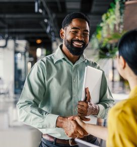 Two people shaking hands in an office with a laptop.