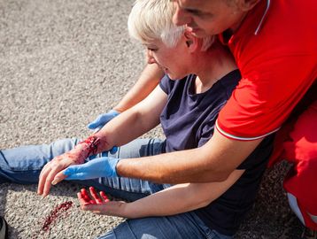 Person with arm injury receiving aid outdoors.