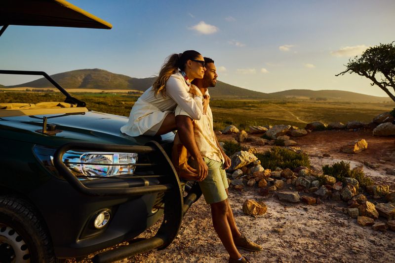 Young adult couple relaxing on safari vehicle, admiring the vast landscape at sunset