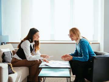 Two women discussing documents in a bright office setting.