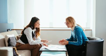 Two women discussing documents in a bright room.