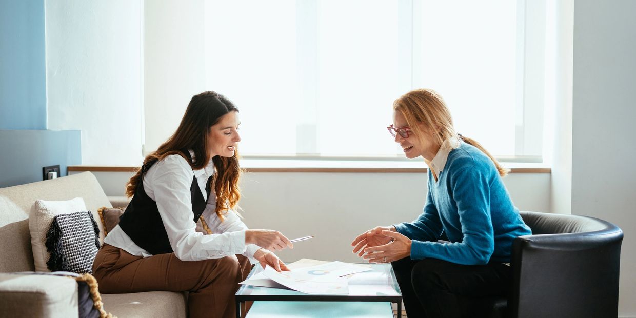 Two women discussing documents in a bright office setting.