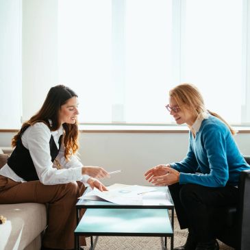 Two women discussing documents in a bright office setting.