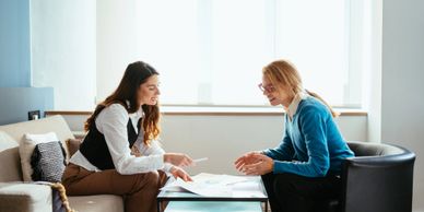 Two women discussing documents in a bright office setting.