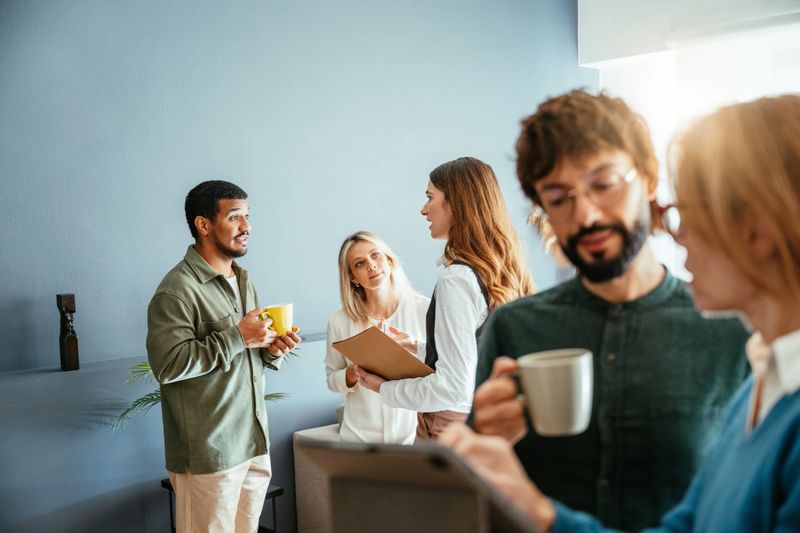 Group of coworkers chatting and laughing during a casual meeting in a modern office setting with relaxed atmosphere