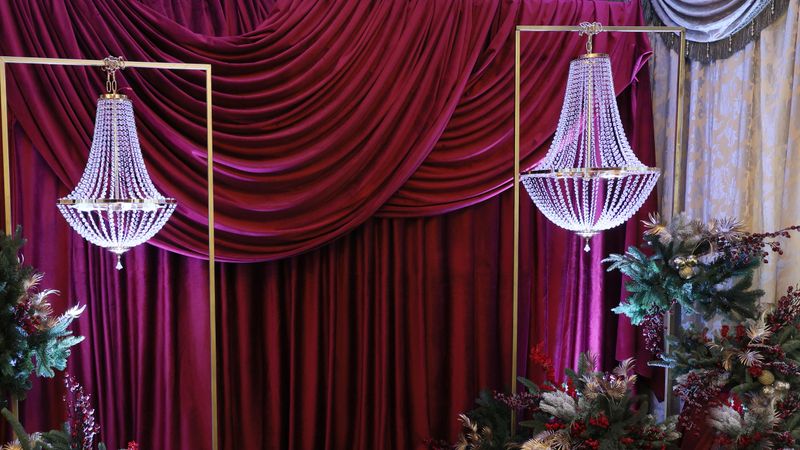 A festive interior featuring two crystal chandeliers and fir branch decor against a backdrop of red curtains. Holiday concept.