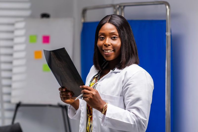 Portrait of African female doctor holding an x-ray image and smiling at camera in hospital