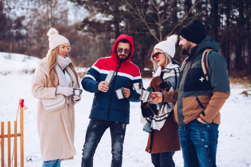 Group of friends enjoying a warm drink from a thermos bottle in a snowy forest