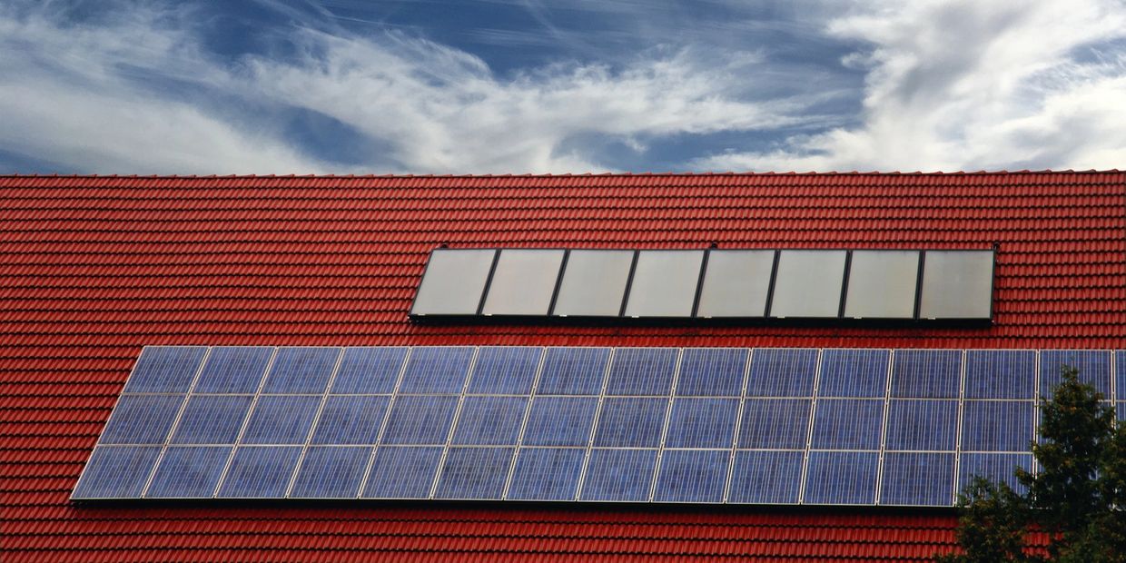 Solar panels installed on a red-tiled roof under a partly cloudy blue sky.