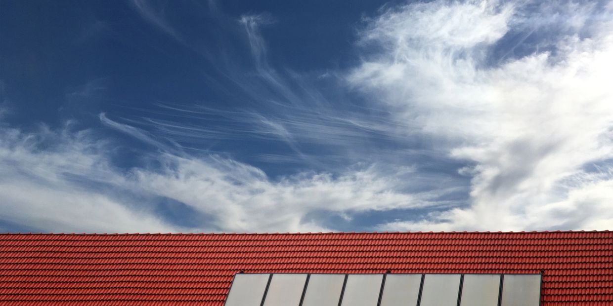 Solar panels installed on a red-tiled roof under a partly cloudy blue sky.