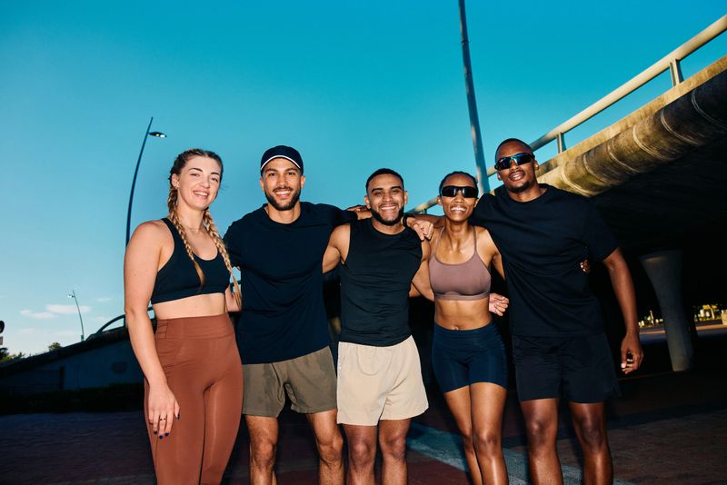 Group portrait of young athletes standing shoulder to shoulder under blue sky after run, showing confidence, teamwork and strong sense of running community.