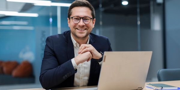 Smiling man sitting at a desk with a laptop.