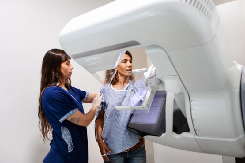 Young female radiology technician explaining and performing a breast exam on a middle-aged female patient using a state-of-the-art mammography machine in a medical clinic - Buenos Aires - Argentina