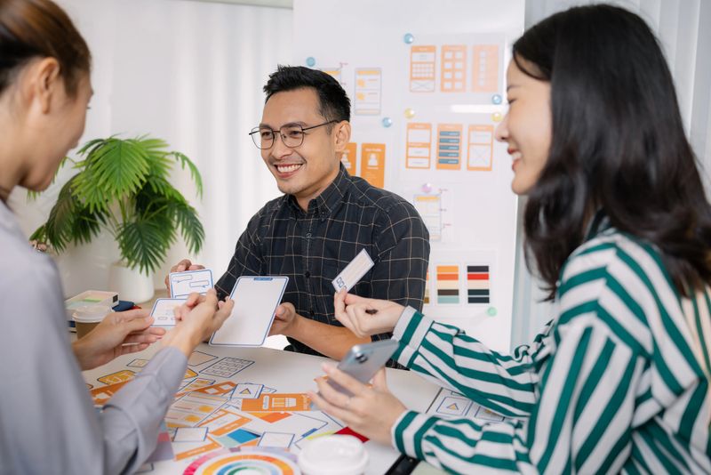 A group of UX/UI designers brainstorming creative ideas together, discussing color palettes and layout concepts for a new mobile application interface in a modern design office.