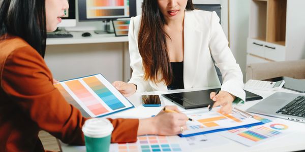 Two women discussing color swatches and charts in a creative meeting.
