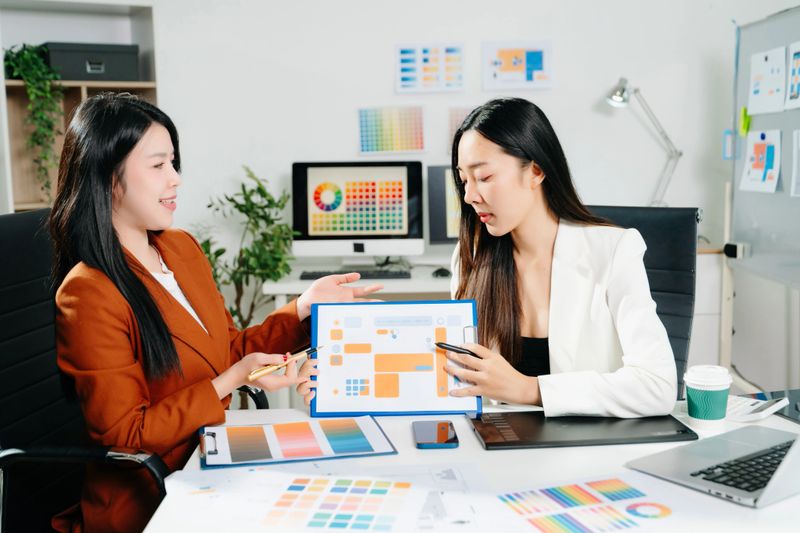 Two professional women designers discussing UX UI and color palette in a creative modern office. Ideal for teamwork, innovation, and digital business themes.