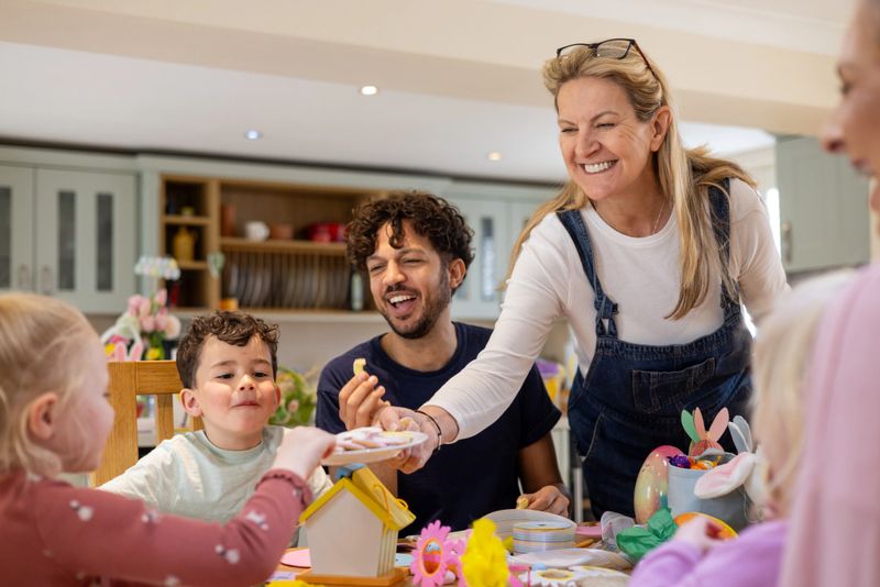 Medium shot of a group of adults and children gathered in the kitchen of a home in Northumberland, North East England. There is an Easter display on the table, including craft supplies which the children are using. A mature adult female is offering a plate of biscuits to the children.Videos similar to this scenario available.