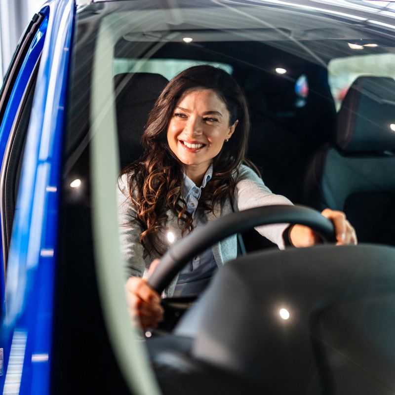 Smiling woman experiencing a car in a showroom. She is happy sitting in the driver's seat, holding the steering wheel