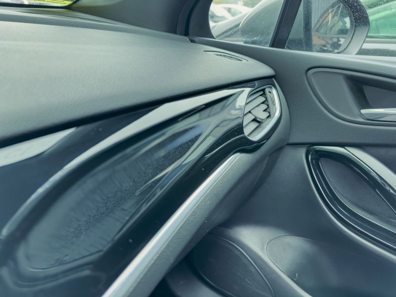 Detailed focus on a car's interior, highlighting smooth surfaces, stylish air vents, and refined materials while parked in a lot under overcast skies.